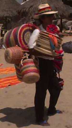 A picture of a man carrying hats, baskets, almost anything that can be made out of straw.